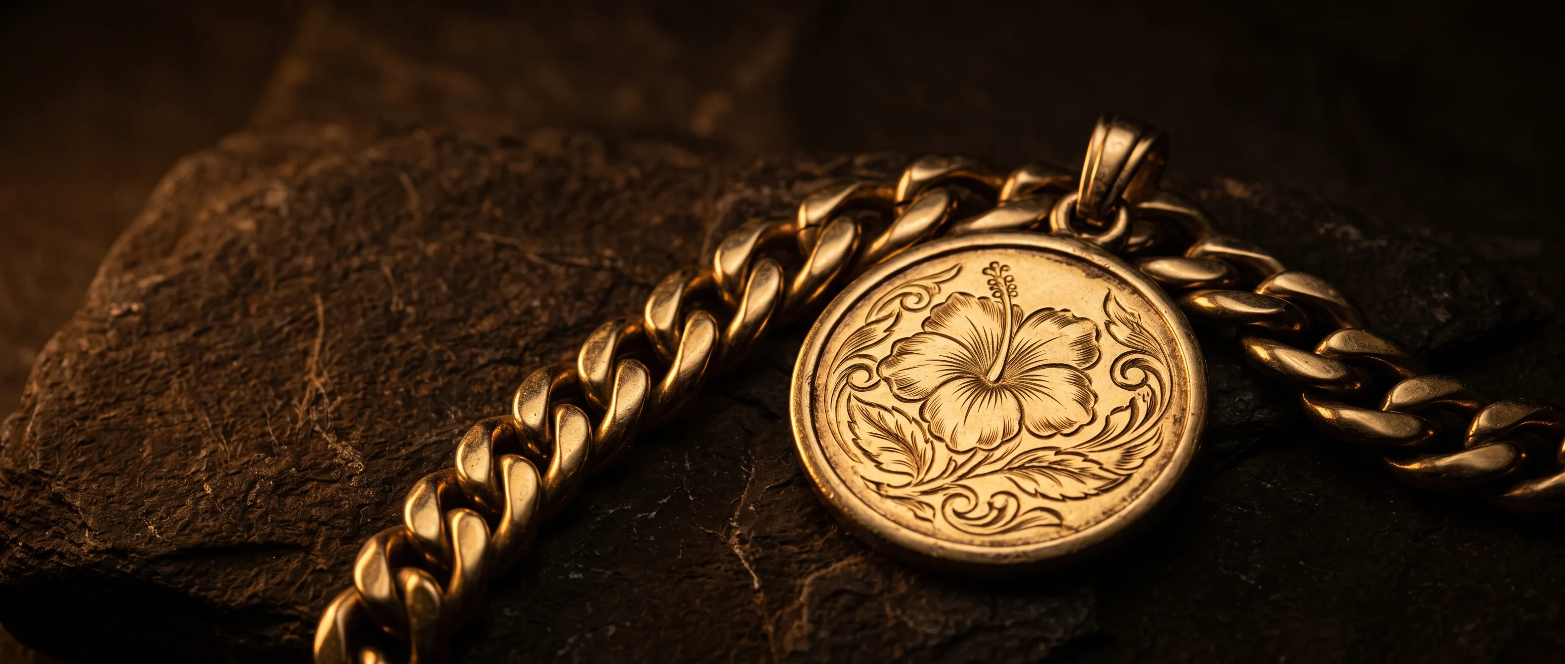 Chaîne en or et médaille gravée d'un hibiscus sur pierre sombre
