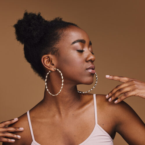 Black woman, pose or fashion hairstyle on isolated brown background in relax self love, trendy or cool style promotion. Confident, hands or beauty model with makeup cosmetics, natural hair or jewelry.