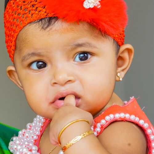 A small, adorable baby girl is licking her finger in this heartwarming stock photo.